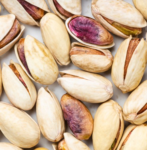 square food background - shelled and ripe pistachio nuts close up